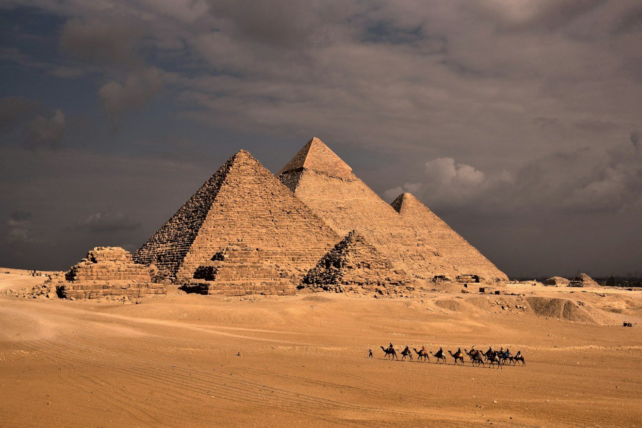 A camel caravan crossing the desert at sunset beside the Great Pyramid